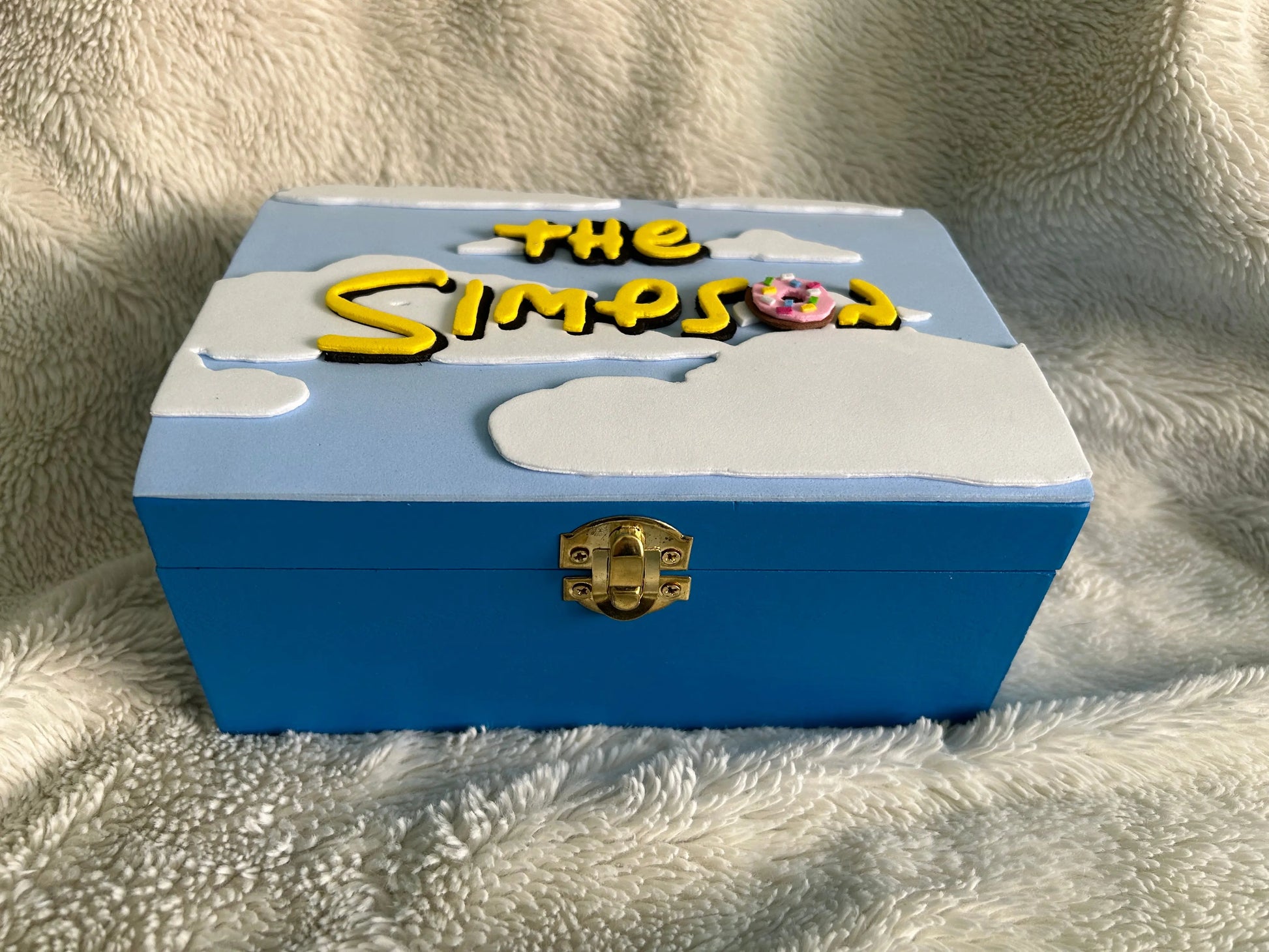 Blue wooden decorative box with raised white clouds and "The Simpson" text featuring a donut, handcrafted for fans of The Simpsons.