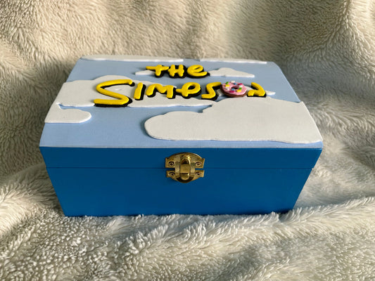 Blue wooden decorative box with raised white clouds and "The Simpson" text featuring a donut, handcrafted for fans of The Simpsons.