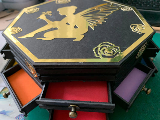 Black handcrafted wooden Joyero Hada Mágica jewelry organizer with gold fairy design on top and colorful open drawers.